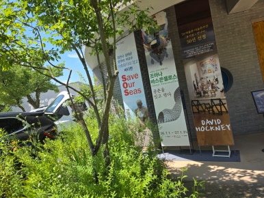 초록 나무와 전시 현수막이 보이는 양평 구하우스 미술관 본관 입구